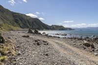 an empty beach with mountains on a sunny day near the ocean and water with stones