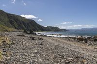 an empty beach with mountains on a sunny day near the ocean and water with stones