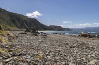 an empty beach with mountains on a sunny day near the ocean and water with stones