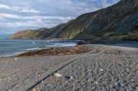 the view of a mountain and a beach from the shoreline of a rocky coastline