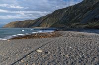 the view of a mountain and a beach from the shoreline of a rocky coastline