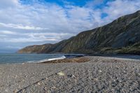 the view of a mountain and a beach from the shoreline of a rocky coastline