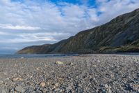 the view of a mountain and a beach from the shoreline of a rocky coastline