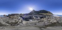 an island is seen through a fisheye lens with the sun rising over rocks and water