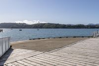 the boardwalk is leading towards the water to a pier next to some boats on the beach