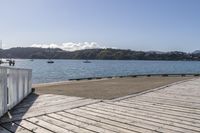 the boardwalk is leading towards the water to a pier next to some boats on the beach