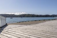 the boardwalk is leading towards the water to a pier next to some boats on the beach