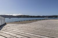 the boardwalk is leading towards the water to a pier next to some boats on the beach