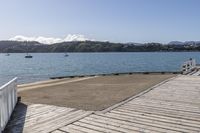 the boardwalk is leading towards the water to a pier next to some boats on the beach