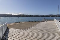 the boardwalk is leading towards the water to a pier next to some boats on the beach