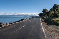 a lone empty asphalt road by the water and some rocks under a blue sky and clouds