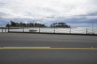 a road and a fence along side a large body of water on a cloudy day