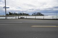 a road and a fence along side a large body of water on a cloudy day