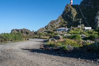 a gravel road in front of a hill with a light tower on top and another hill