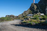 a gravel road in front of a hill with a light tower on top and another hill