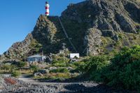 a large mountain with a white lighthouse on it's side and a red house underneath it