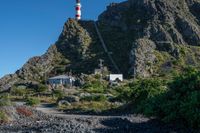 a large mountain with a white lighthouse on it's side and a red house underneath it