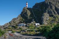 a large mountain with a white lighthouse on it's side and a red house underneath it