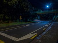 an empty street near a bridge with street lights lit up at night for the camera