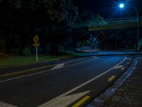 an empty street near a bridge with street lights lit up at night for the camera