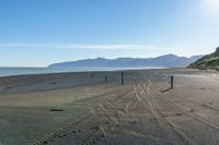 tracks and signs are on the beach near the water with mountains in the distance and blue skies