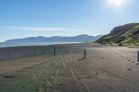 tracks and signs are on the beach near the water with mountains in the distance and blue skies