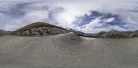 a panorama lens lensing a view of a desert, with sparse areas of dirt, sand and mountains