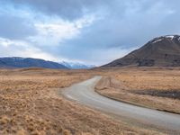 a large empty road in a very deserted area with snow capped mountains in the background