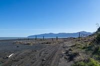 a large dirt road with tire tracks on the ground and mountains in the background with water