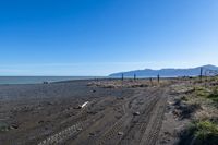 a large dirt road with tire tracks on the ground and mountains in the background with water
