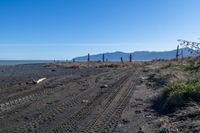 a large dirt road with tire tracks on the ground and mountains in the background with water