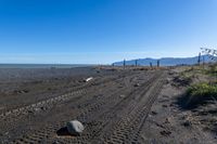 a large dirt road with tire tracks on the ground and mountains in the background with water