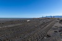 a large dirt road with tire tracks on the ground and mountains in the background with water