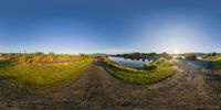 a panoramic shot of a dirt road with trees and the sun shining over water