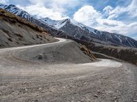 a road winding with snow capped mountains in the distance, and dirt road winding at the foreground