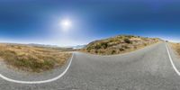 an asphalt road going up a hill, with a bright sun in the sky above