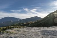 a man riding on top of a grass covered hillside next to mountains and clouds,