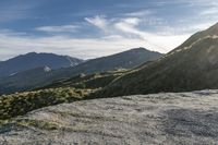 a man riding on top of a grass covered hillside next to mountains and clouds,