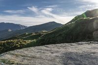 a man riding on top of a grass covered hillside next to mountains and clouds,