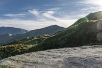 a man riding on top of a grass covered hillside next to mountains and clouds,