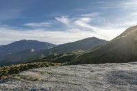 a man riding on top of a grass covered hillside next to mountains and clouds,