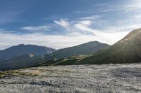 a man riding on top of a grass covered hillside next to mountains and clouds,