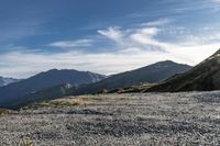 a man riding on top of a grass covered hillside next to mountains and clouds,