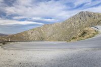 a car driving on a curved road next to mountains with clouds over a ridge in the background