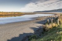 a small sandy beach area and a few poles on the water's edge with hills in the background