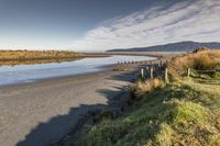 a small sandy beach area and a few poles on the water's edge with hills in the background