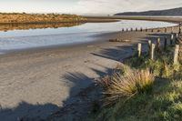 a small sandy beach area and a few poles on the water's edge with hills in the background