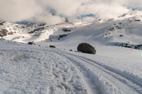 a lone snow skier making his way up a snowy mountain slope with large rocks in the distance