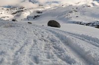 a lone snow skier making his way up a snowy mountain slope with large rocks in the distance