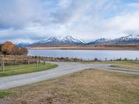 a park bench near a dirt road in an empty field near a lake and mountains